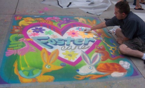 Roger Whiting painting a chalk mural of a heart with "Foster Care" written on the inside